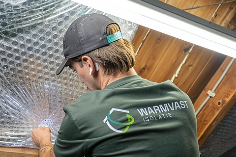 Warmvast-monteur bevestigt reflecterende isolatiefolie tussen de dakspanten